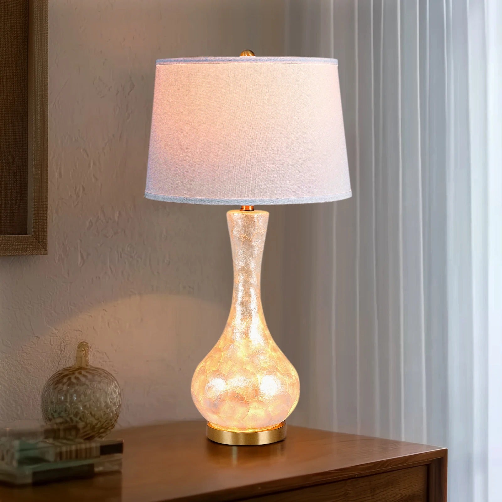 Luxury table lamp with shell body and linen shade on bedside table